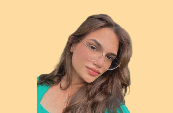 foto da colabora Paula, em um fundo amarelo pastel, uma mulher branca, de 19 anos, cabelos castanhos claros e olhos castannhos, usa óculos, olhando para a câmera com um leve sorriso e cabeça levemente inclinada